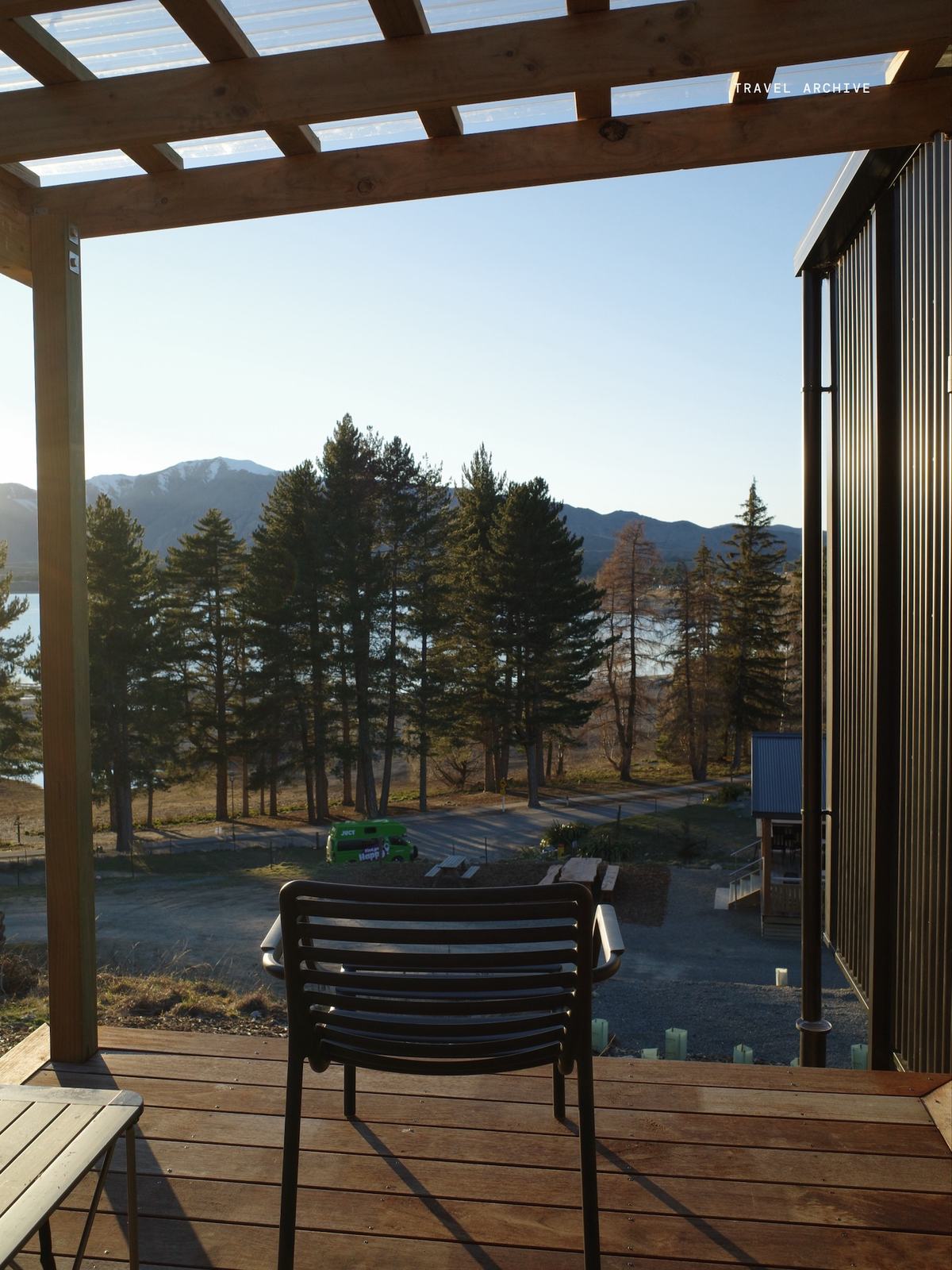 A deck looking out over pines, a lake and the Canterbury foothills at golden hour